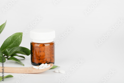 Herbal pills in glass bottle, wooden spoon and green plant on white background. alternative medicine and healthy lifestyle concept. copy space photo