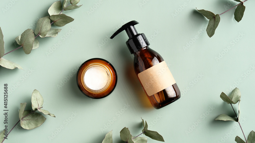 Skincare cosmetics products and eucalyptus leaves on green background top view. Flat lay jar of moisturizer cream and natural herbal shower gel in amber glass dispenser bottle. SPA treatment concept. Skincare cosmetics products and eucalyptus leaves on green background top view. Flat lay jar of moisturizer cream and natural herbal shower gel in amber glass dispenser bottle. SPA treatment concept.