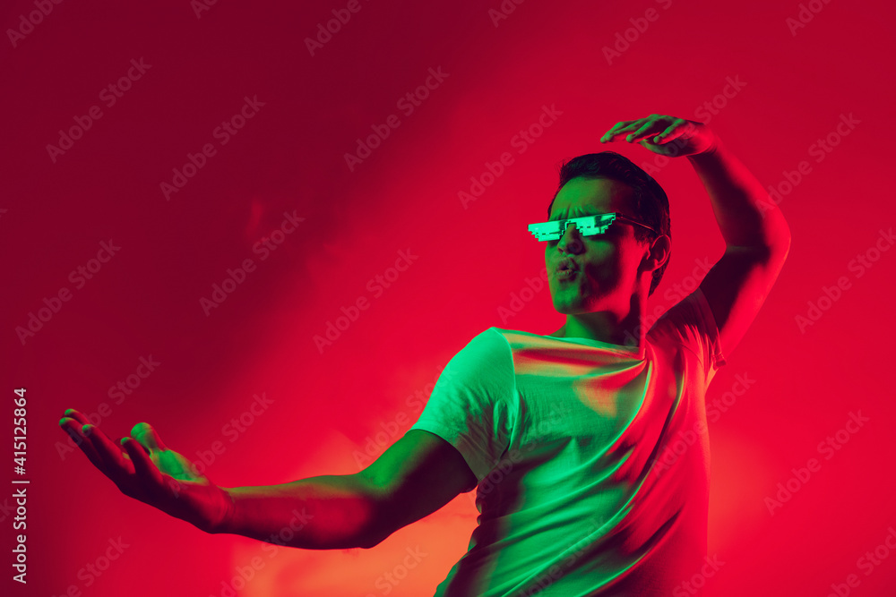 Stylish. Caucasian man's portrait isolated on red studio background in multicolored neon light. Beautiful male model. Concept of human emotions, facial expression, sales, ad, fashion. Copyspace. Stylish. Caucasian man's portrait isolated on red studio background in multicolored neon light. Beautiful male model. Concept of human emotions, facial expression, sales, ad, fashion. Copyspace.