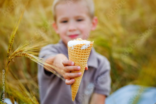Selective focus. Ice cream cone in the hands of a boy who is sitting in a wheat field on a picnic. Summer mood.