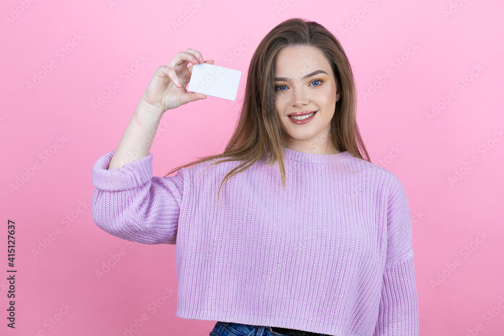 Young pretty woman with long hair standing over isolated pink background smiling and holding white card Young pretty woman with long hair standing over isolated pink background smiling and holding white card