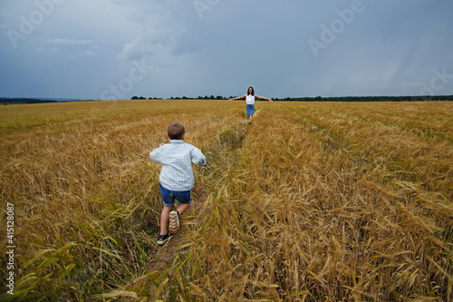 A happy family of mother and son in a summer wheat field. The son runs to meet the mother, and she opens her arms for a hug. Rural landscape