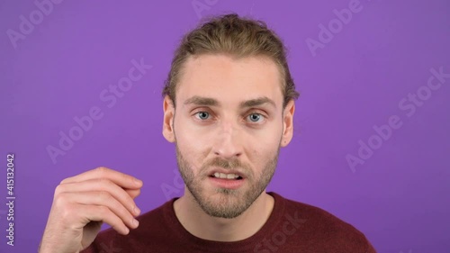 young aggressive long-haired guy showing blah blah gesture on isolated purple background. Sarcastic face. 4k photo