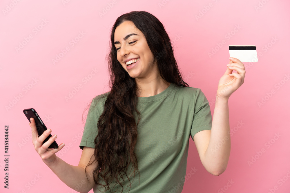 Young caucasian woman isolated on pink background buying with the mobile with a credit card Young caucasian woman isolated on pink background buying with the mobile with a credit card