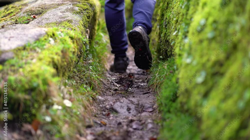 Man in blue pants and boots, passing by a path between two rocks full of moss, and surrounded by vegetation, with leaves on the ground, in a forest in Spain. Lifestyle concept Man in blue pants and boots, passing by a path between two rocks full of moss, and surrounded by vegetation, with leaves on the ground, in a forest in Spain. Lifestyle concept