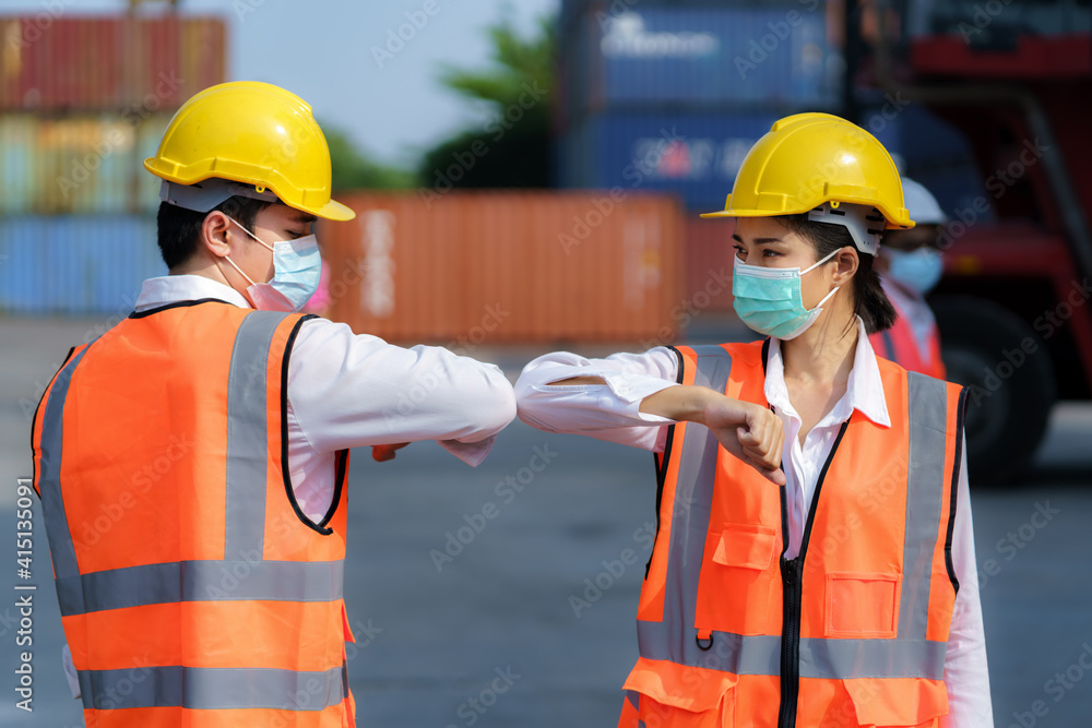 Asian worker new normal greeting by elbows bump wear safety helmet and mask in container depot terminal for prevent coronavirus and social distancing concept.. Asian worker new normal greeting by elbows bump wear safety helmet and mask in container depot terminal for prevent coronavirus and social distancing concept..