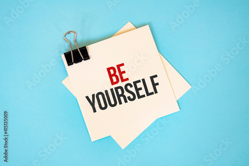 Text Be yourself on sticky notes with copy space and paper clip isolated on red background.Finance and economics concept.