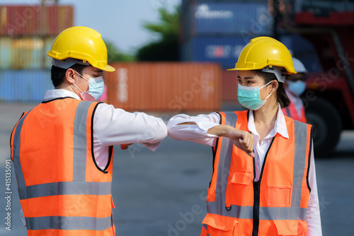Asian worker new normal greeting by elbows bump wear safety helmet and mask in container depot terminal for prevent coronavirus and social distancing concept..