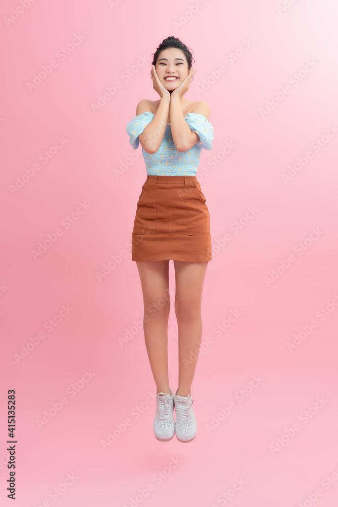 Full length portrait of a joyful young woman jumping and celebrating over pink background Full length portrait of a joyful young woman jumping and celebrating over pink background
