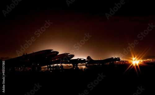 Flight line of historical aircraft at the Sun and Fun Fly In air show in Lakeland, Florida.  Planes silhouetted in the dark lit by airport lighting.