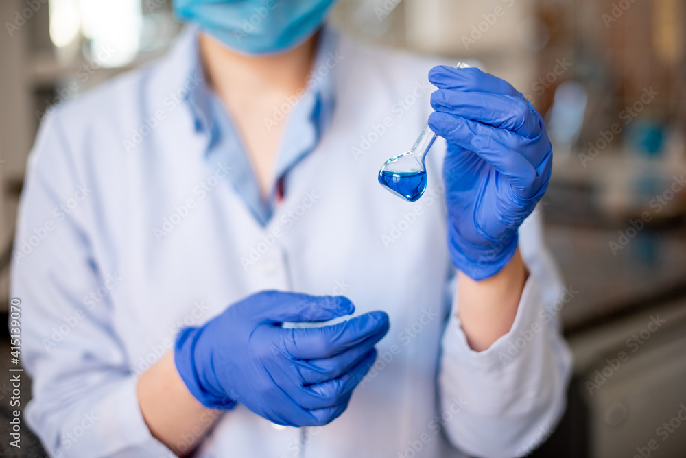 Scientist researching in laboratory. Focused female science professional holding blue solution into the glass cuvette. Healthcare and biotechnology concept. Scientist researching in laboratory. Focused female science professional holding blue solution into the glass cuvette. Healthcare and biotechnology concept.