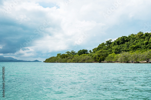 Tropical island with a palm trees with a crystal clear blue sea water and cloudy sky.