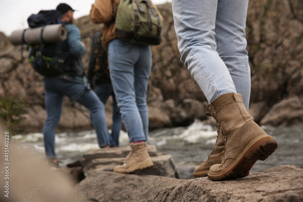 Group of friends with backpacks crossing mountain river, focus on hiking boots Group of friends with backpacks crossing mountain river, focus on hiking boots