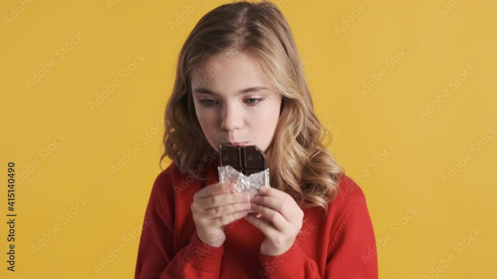 Beautiful blond teenage girl greedily eating chocolate over yellow background. Sweet tooth girl Beautiful blond teenage girl greedily eating chocolate over yellow background. Sweet tooth girl