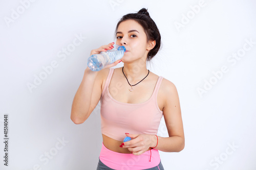 Brunette girl drinks water in sports uniform after training. White background. Portrait. Health