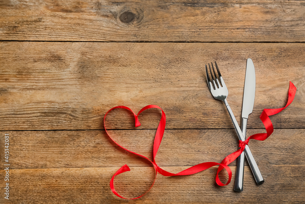 Cutlery set and red ribbon on wooden background, flat lay with space for text. Valentine's Day dinner Cutlery set and red ribbon on wooden background, flat lay with space for text. Valentine's Day dinner