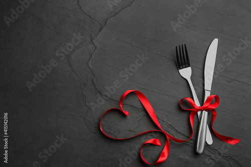 Cutlery set and red ribbon on black background, flat lay with space for text. Valentine's Day dinner