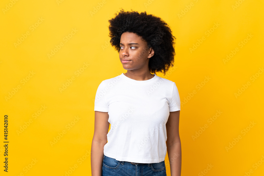 Young African American woman isolated on yellow background making doubts gesture looking side Young African American woman isolated on yellow background making doubts gesture looking side