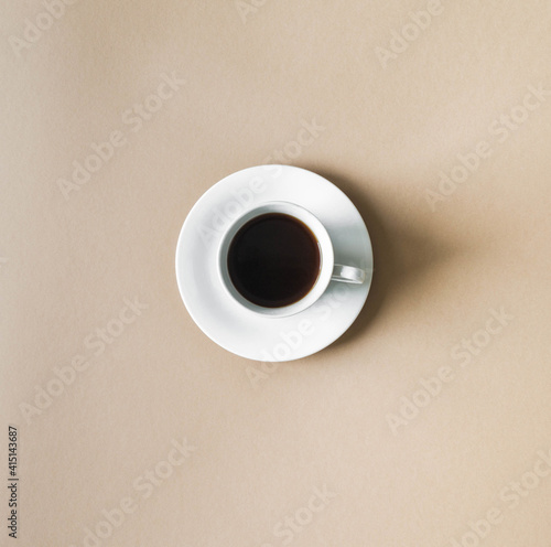 White cup and saucer with black coffee on beige background