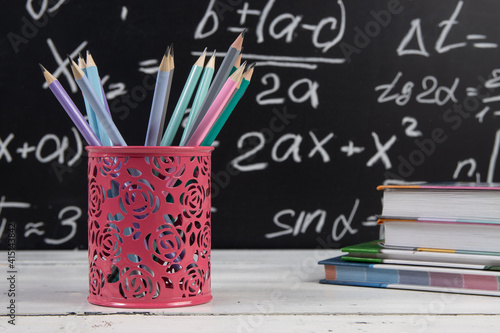 Pencils and books on blackboard background with mathematical formulas. Education concept.