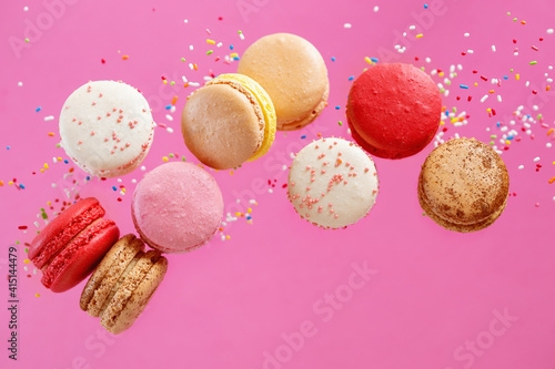 Colorful macarons and sugar sprinkles on pink background