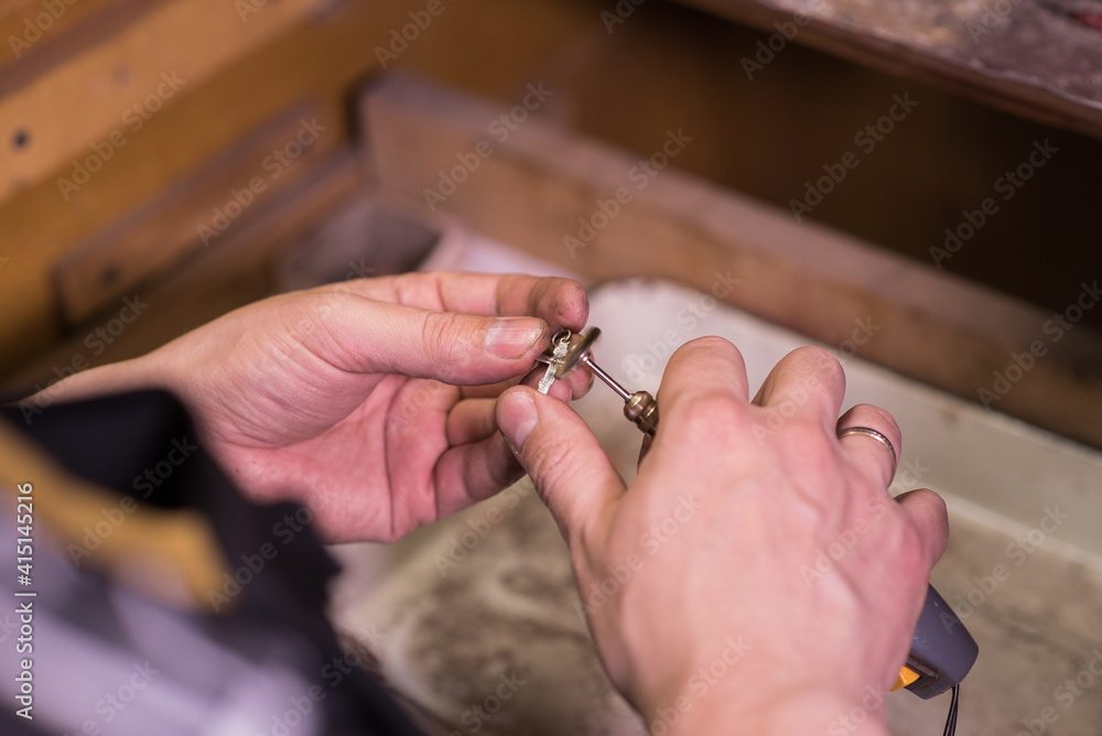 Hands of a jeweler who grinds a silver chain with a cross