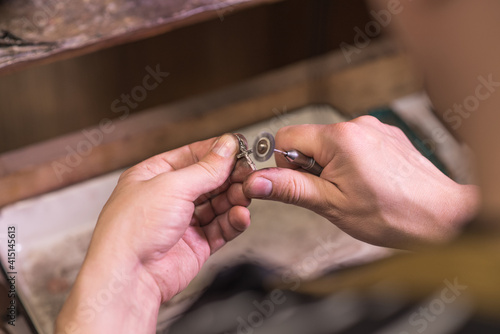 Hands of a jeweler who grinds a silver chain with a cross