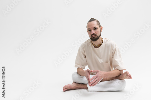 Relaxed young man in white cloath sitting on studio floor isolated on white background photo
