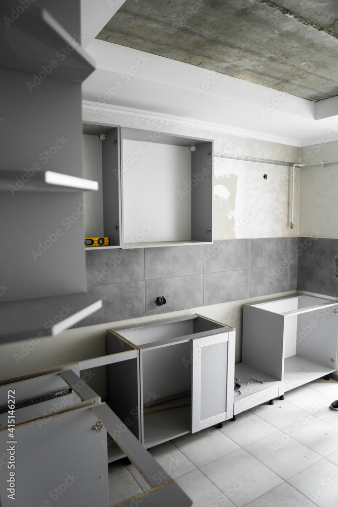 Custom kitchen cabinets installation without a furniture facades mdf. Gray modular kitchen from chipboard material on a various stages of installation in kitchen with a grey tile on floor and walls. Custom kitchen cabinets installation without a furniture facades mdf. Gray modular kitchen from chipboard material on a various stages of installation in kitchen with a grey tile on floor and walls.