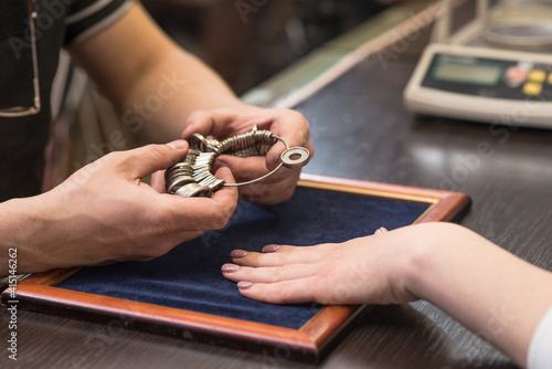 The hands of the jeweler who put the finger ring on the client's hand. Jeweler checks looks the size of the ring