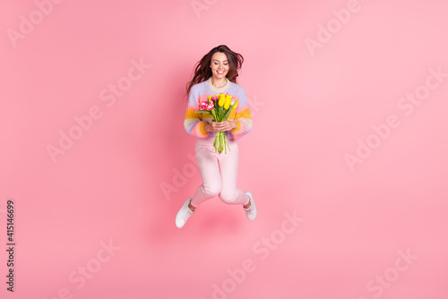 Full length body size view of lovely trendy cheerful girl jumping holding fresh tulips season event isolated over pink pastel color background