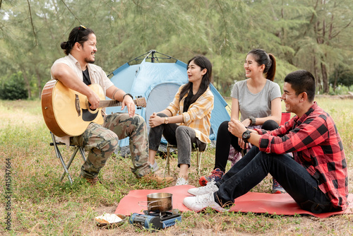 jungle camping concept, four Asian men and women chatting. Party beside the tent, picnic and camping have fun.