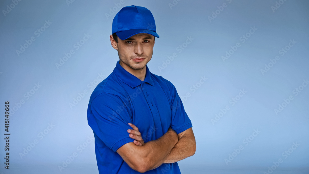 confident delivery man standing with crossed arms isolated on blue confident delivery man standing with crossed arms isolated on blue