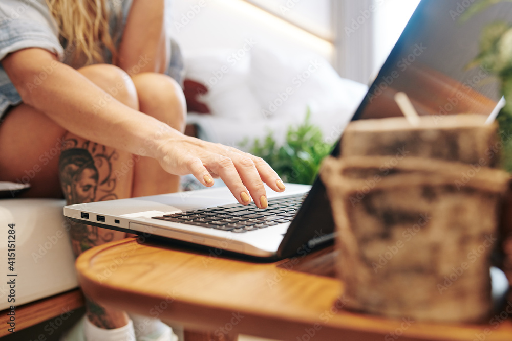 Close-up image of young woman sitting sofa and pushing button on laptop Close-up image of young woman sitting sofa and pushing button on laptop