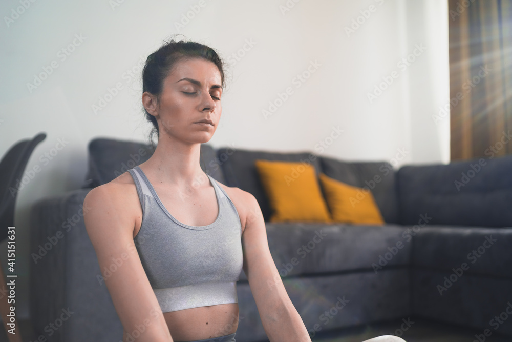 Close look of meditating woman in grey sportswear sitting on floor at home