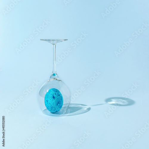 Easter egg standing upright, protected under a transparent wine glass. Concept of holidays during the pandemic isolation times.