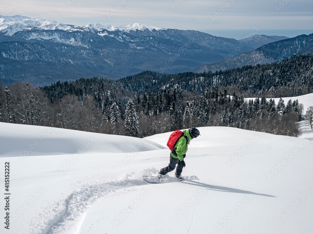 Active man riding snowboard on powder snow at mountains, forest and sea background in Krasnaya Polyana, Russia