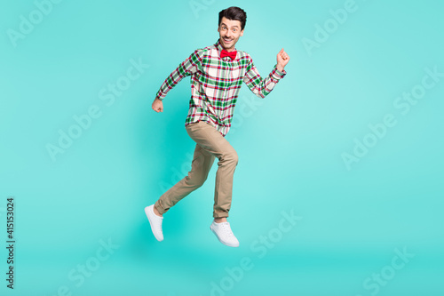 Photo of crazy guy jump run fast look camera wear checkered shirt bow tie isolated blue color background © deagreez