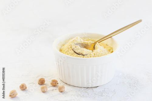 Chickpea flour in a white bowl with a spoon on a light background.