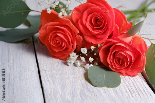Beautiful coral roses and eucalyptus on a white wooden table. Holiday concept and copy space.