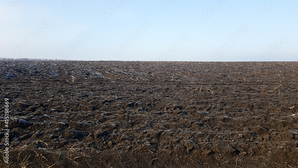 Agricultural field plowed by tractors under blue sky. The field has been plowed, crops have been sown. Close up of soil texture. Rural scene. Farming and food industry. Arable land of chernozem.