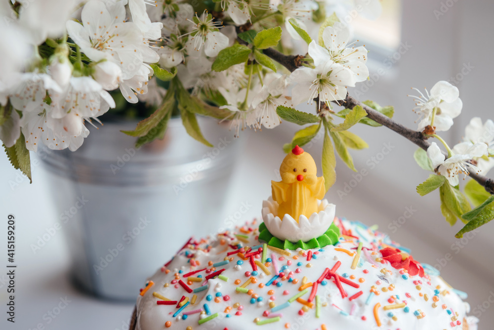 Easter cake decorated with icing baby chick and sugar pearl sprinkles with blossoming tree branches on the background