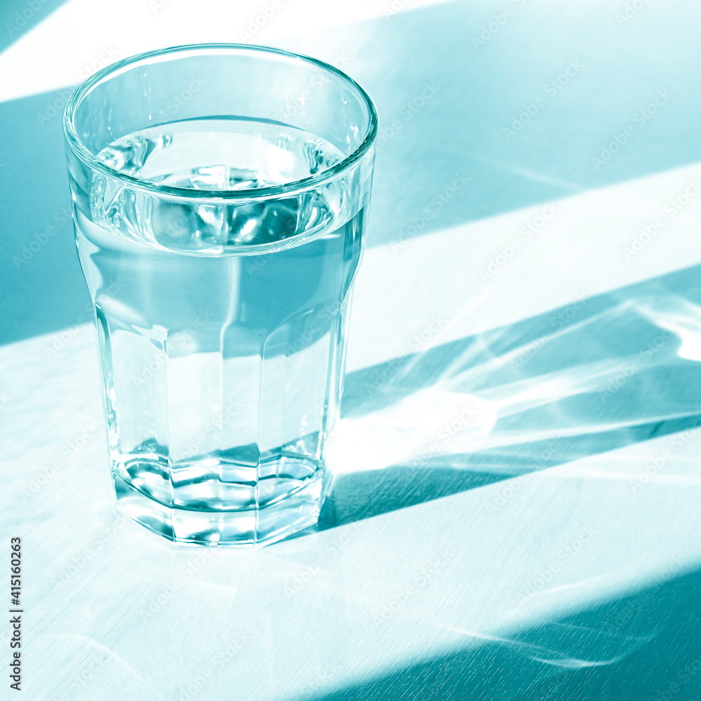 A glass with clean clear water and sharp shadows stands on a white table A glass with clean clear water and sharp shadows stands on a white table