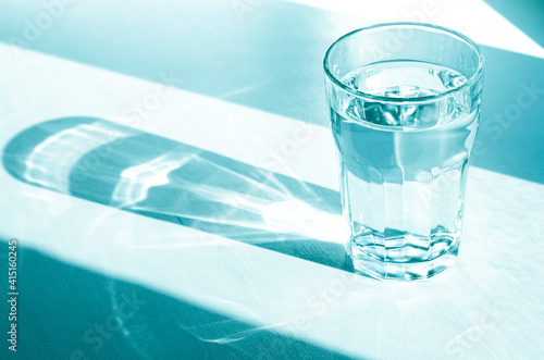 A glass with clean clear water and sharp shadows stands on a white table