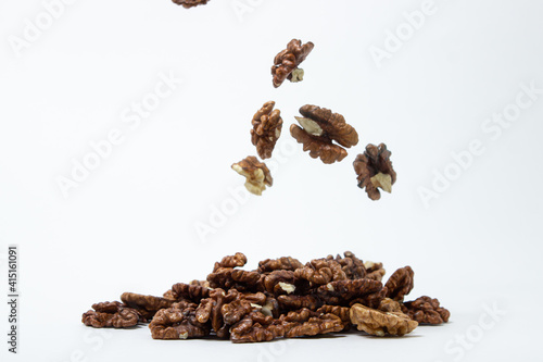 Peeled walnuts on a white background. A peeled walnut falls down onto a pile of walnuts. Nutritious food