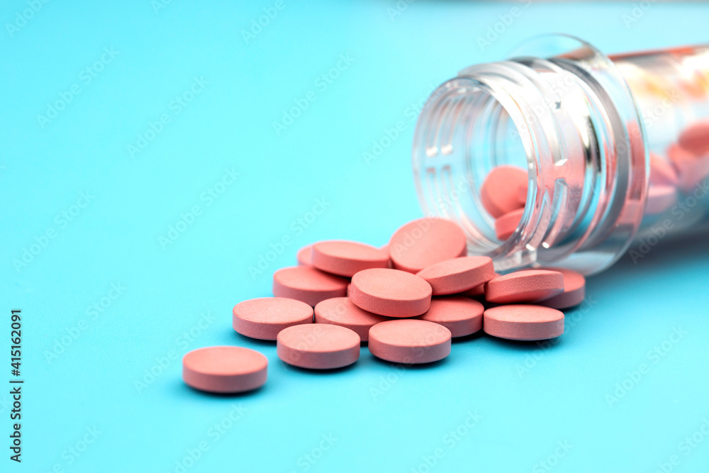 Pink pills pouring out of the medicine container on a blue background. Pink pills pouring out of the medicine container on a blue background.