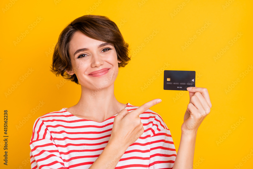 Photo of young attractive happy cheerful smiling girl recommending credit card isolated on yellow color background Photo of young attractive happy cheerful smiling girl recommending credit card isolated on yellow color background