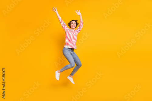Full size photo of optimistic brunette lady jump wear red shirt jeans sneakers isolated on orange color background