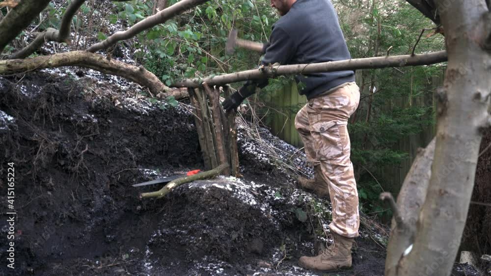 A man hammering logs building a wooden tree structure in soil wearing work clothes A man hammering logs building a wooden tree structure in soil wearing work clothes