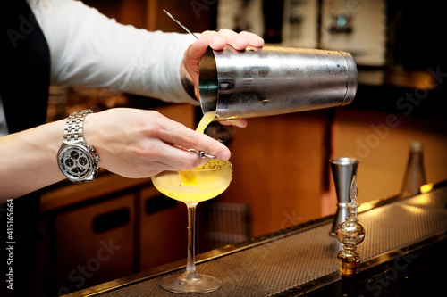 Bartender is pouring cocktail from shaker  toned